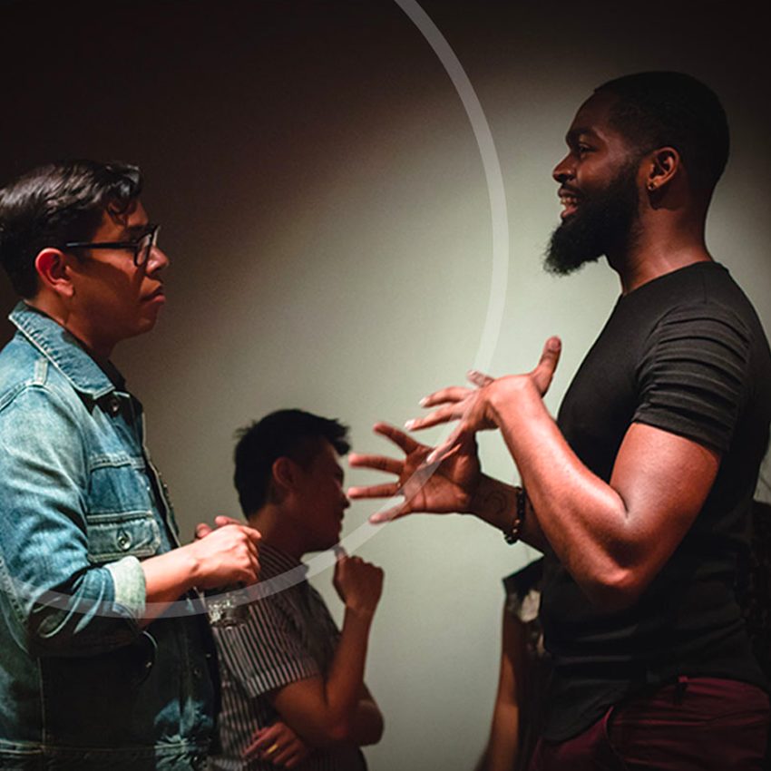 Two Drama League fellows speaking and using hand motions in a dark room